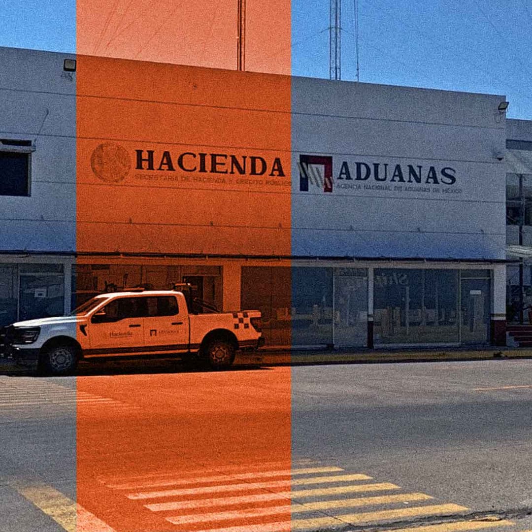 Detrás de una camioneta blanca hay un edificio blanco con letreros en los que se lee 'Hacienda' y 'Aduanas'.