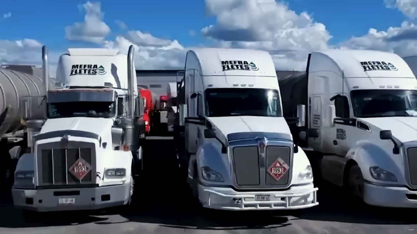 Tres grandes camiones blancos con el logotipo de Mefra Fletes están aparcados uno al lado del otro.